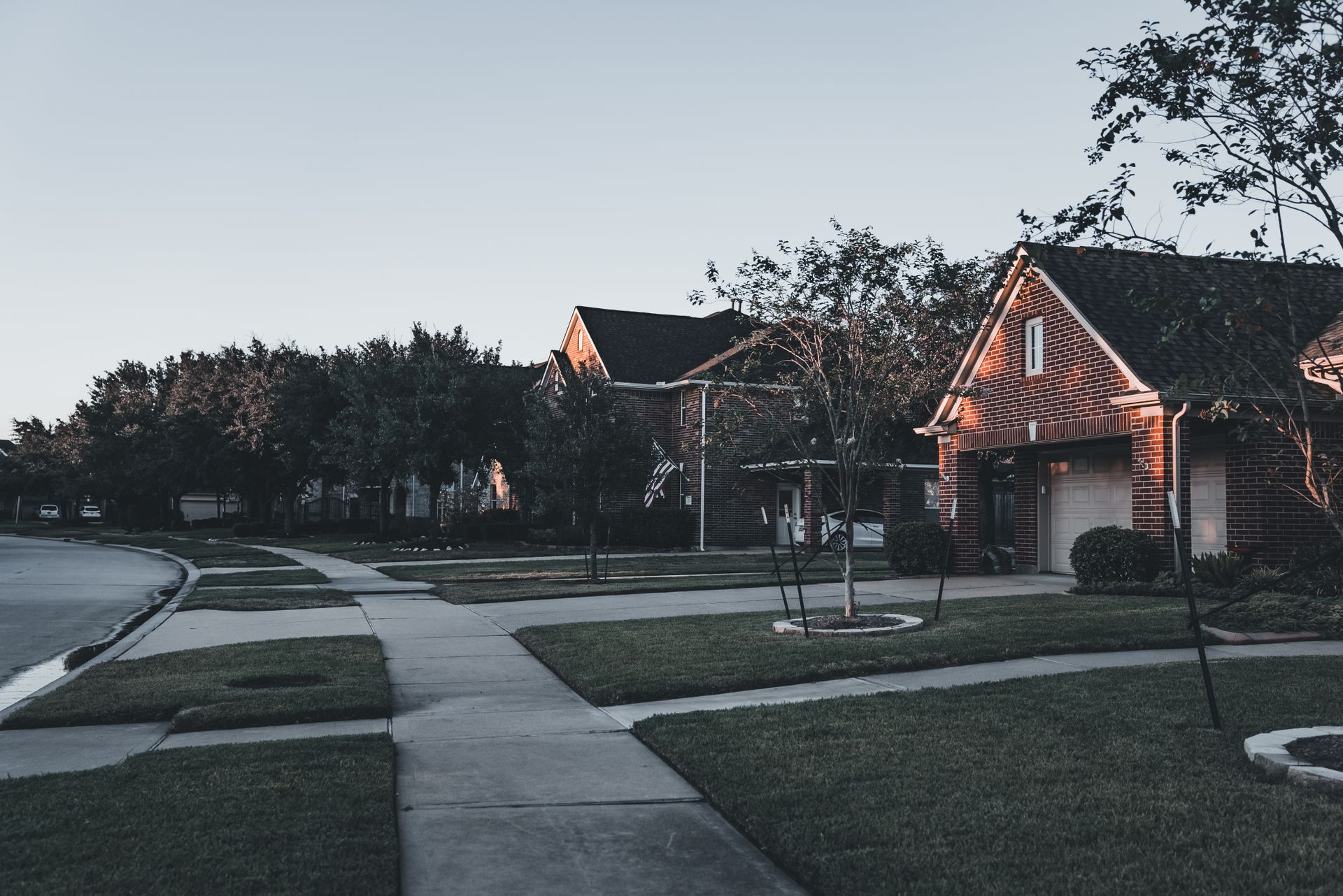 A brick two-story home on a quiet Dallas-area street at dusk.