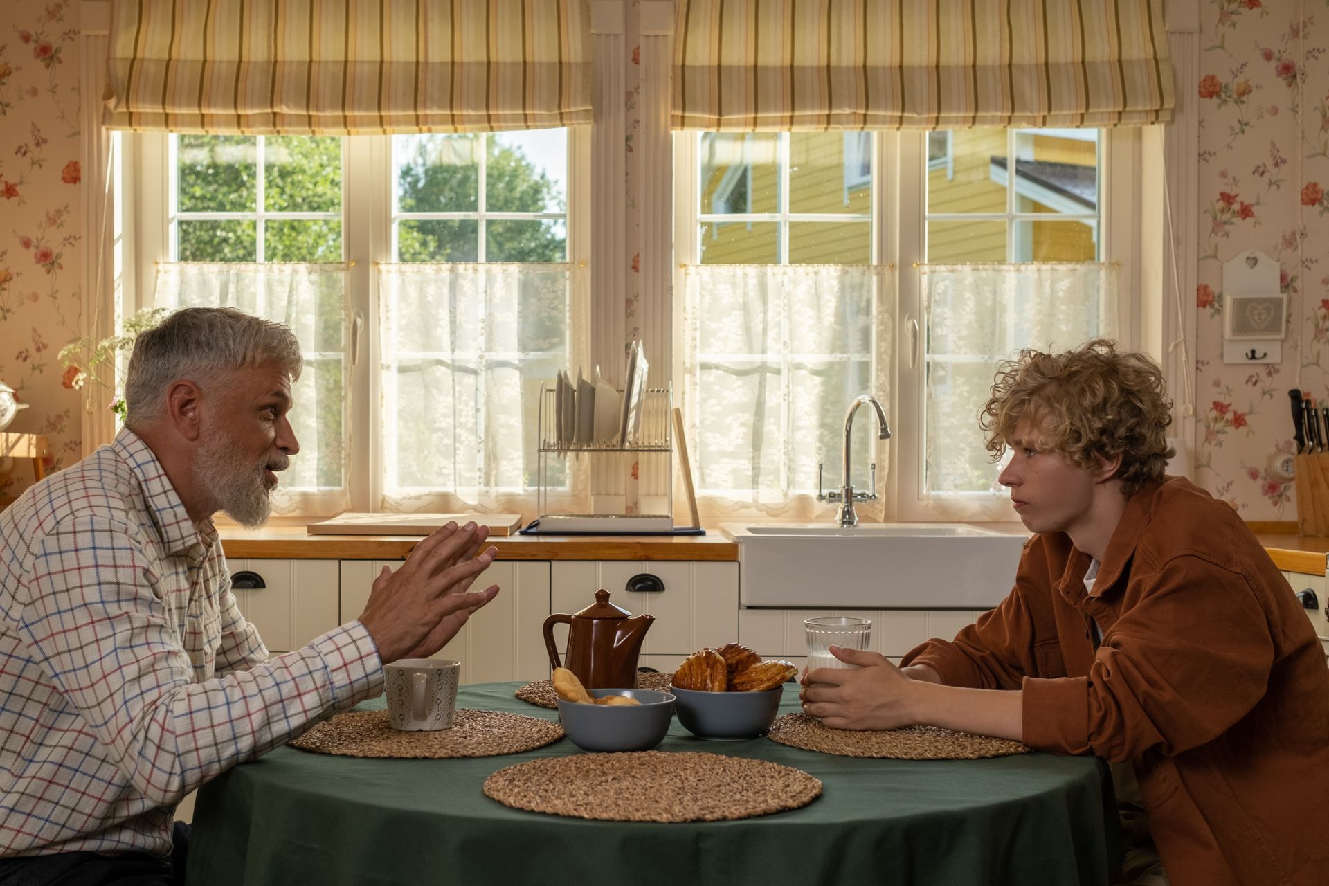 A mentor and client share an animated, eye-contact conversation over coffee at a sunlit kitchen table.
