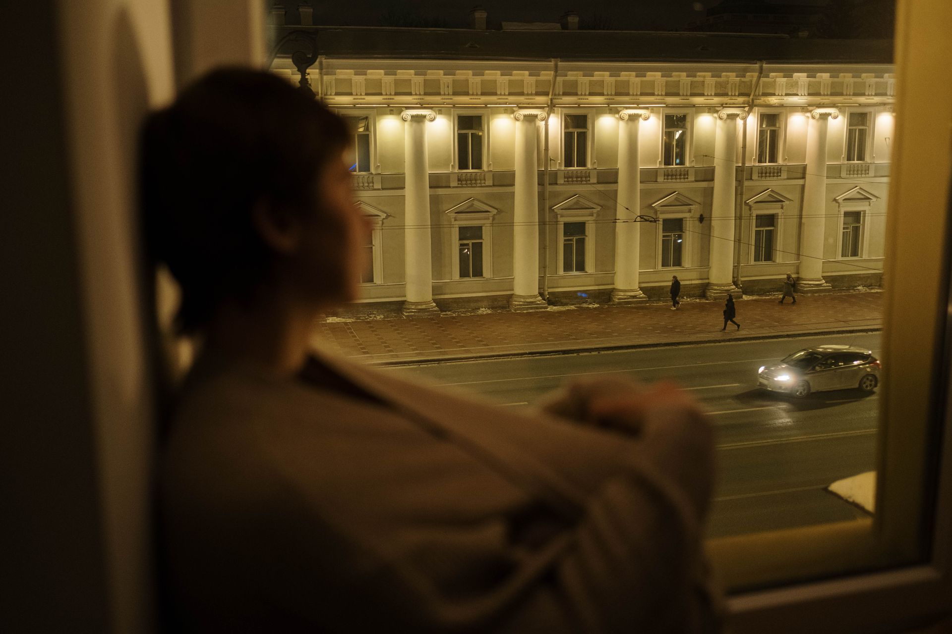 A parent stands at a window late at night, looking out at the quiet street below.