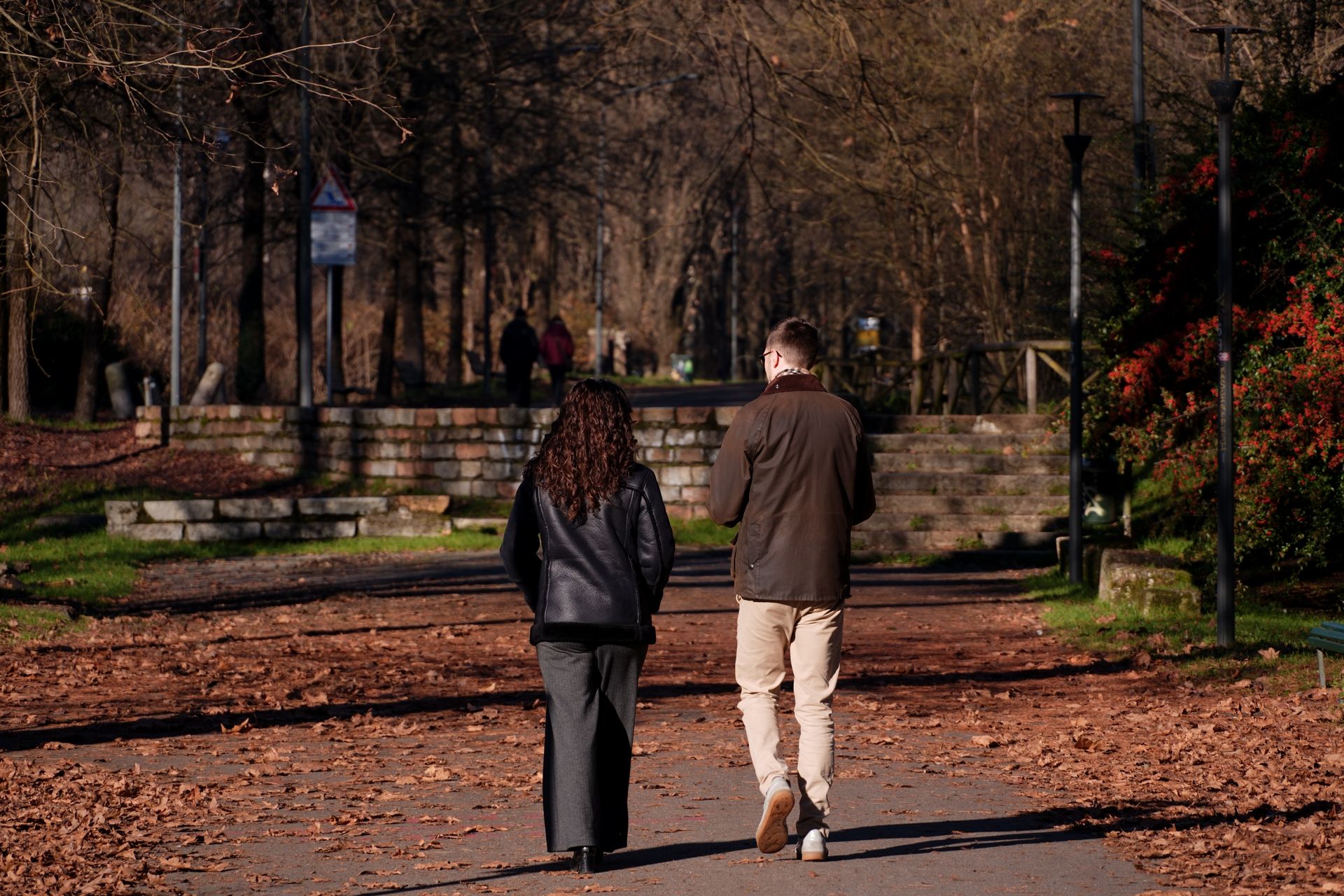 Two people walk together along a quiet, tree-lined path, deep in conversation.