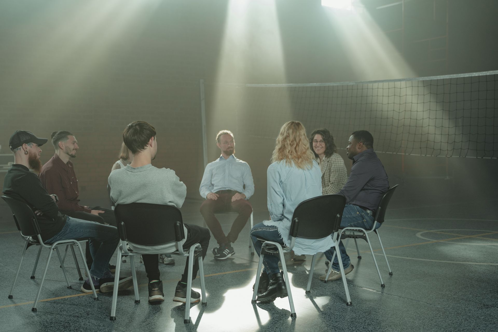 A small support group sits in a circle of chairs in a sunlit room.